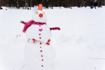 Snowman standing on the background of white snowdrifts in the winter landscape. A lot of snow. Snowwoman.
