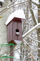 Brown birdhouse on the tree. Handmade wooden nesting box covered in snow. Winter landscape with trees covered of the snow.