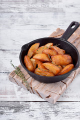 Golden roasted potato wedges in a cast iron pan on white wooden table