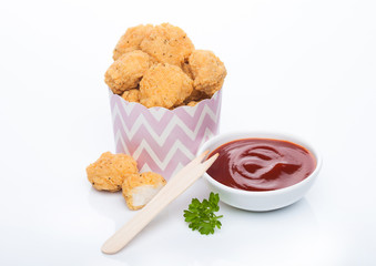 Crunchy chicken popcorn bites in kids paper cup for fast food meals on white background with wooden fork and ketchup.