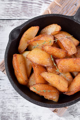 Golden roasted potato wedges in a cast iron pan on white wooden table