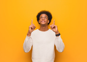Young african american man over an orange wall surprised pointing up to show something