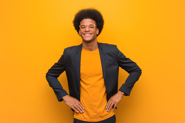 Young business african american man over an orange wall with hands on hips