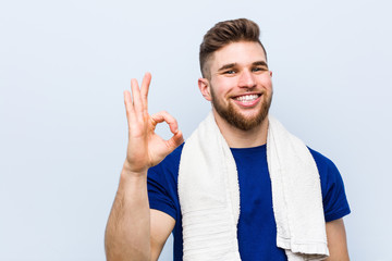Young caucasian sportsman with a towel cheerful and confident showing ok gesture.