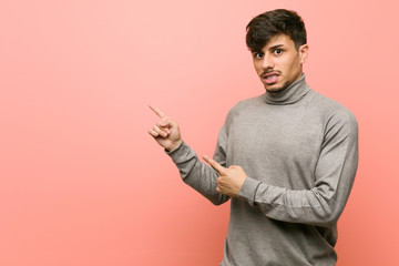 Young smart student man shocked pointing with index fingers to a copy space.