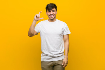 Young hispanic casual man holding something little with forefingers, smiling and confident.