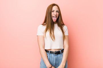 Young redhead ginger woman against a pink wall funny and friendly sticking out tongue.