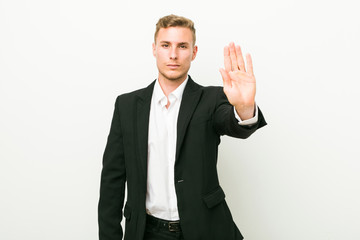 Young caucasian business man standing with outstretched hand showing stop sign, preventing you.