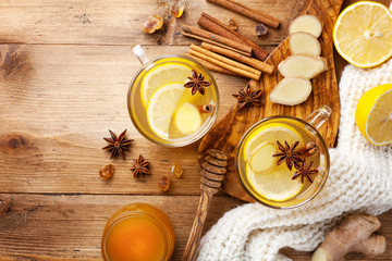 Healing ginger tea in two glass mug in scarf with lemon, honey and spices. Autumn hot drink on rustic wooden table top view.