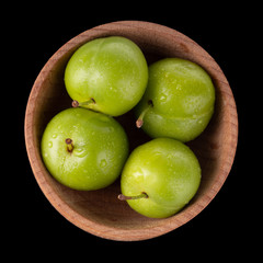heap of green  cherry-plum in wooden cup isolated on black background