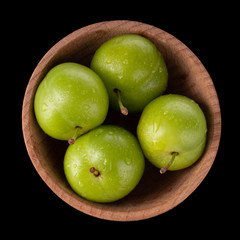 heap of green  cherry-plum in wooden cup isolated on black background