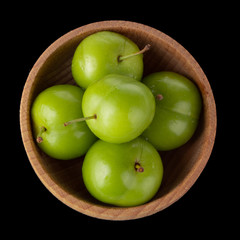 heap of green  cherry-plum in wooden cup isolated on black background