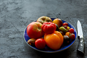  Fresh, ripe cherry on a black background. Different varieties of tomatoes in a plate.