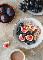 Top view of a breakfast bowl with granola, blue grape and fig slices. Healthy vegan eating flat lay.