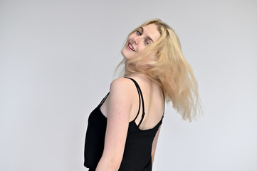 Fototapeta premium Portrait of a cute blonde student girl, a young woman in a black dress with beautiful curly hair on a white background in different poses. Shows hands to the sides. Beauty, brightness, emotions.