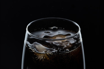 Glass of pouring fizzy drink with ice on a black background