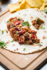 tortilla Chili con carne with corn chips on a wooden cutting board