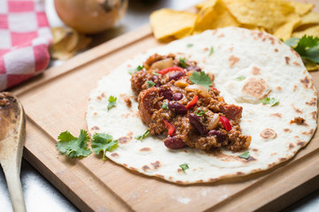 tortilla Chili con carne with corn chips on a wooden cutting board
