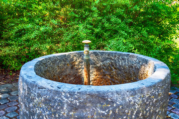 Old water tap with concrete well in the park.