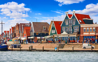 Volendam, Netherlands. Small town fishing village in North Holland near Amsterdam with traditional Houses with Red Tegular Roofs at Waterfront with Docks by Sea.