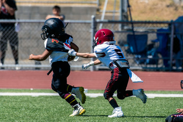 Break away play on youth football game has defensive player grasping the jersey of the escaping offensive athlete.