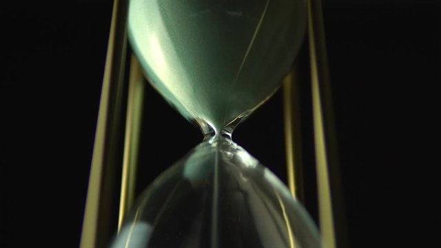 Sand glass grains in the hourglass. Still hour glass close up over black background, transience of time concept. Time of all liveable things idea.