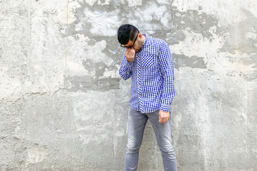 Obraz na płótnie Canvas Portrait of sad depressed alone handsome bearded young man in checkered blue shirt and sunglasses standing against concrete gray wall. holding head down and crying.