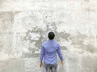 Backside of young man in checkered blue shirt and sunglasses standing against concrete gray wall....