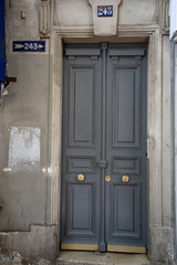 Matte paint grey door with framed panels and shiny brass doorknobs. Grunge textures of weathered stone walls of old building in Paris France. Geometry of rectangular architectural shapes.
