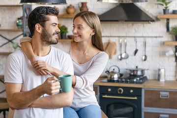 Beautiful young couple embracing in the kitchen at home with look on each other