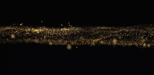 Golden glitter wave, sparkling light particles flow on black background. Glowing gold bokeh light, shimmering dust sparks glow