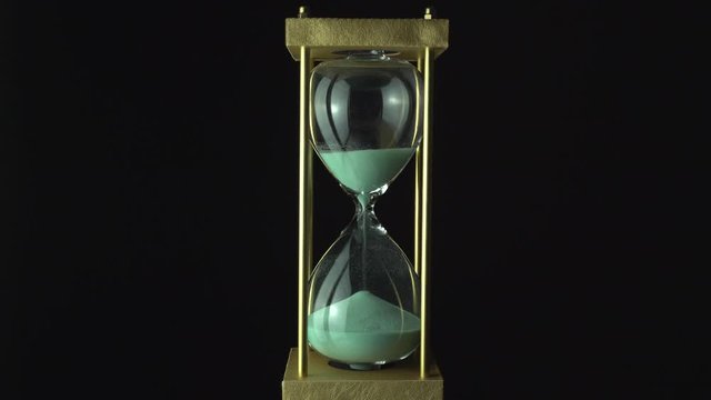 Sand glass grains in the hourglass. Still hour glass close up over black background, transience of time concept. Time of all liveable things idea.