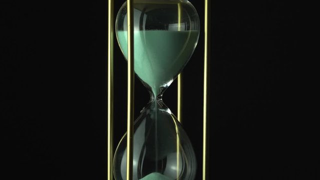 Sand glass grains in the hourglass. Still hour glass close up over black background, transience of time concept. Time of all liveable things idea.