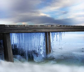 Icicles under wooden jetty in frozen lake on cold winter day