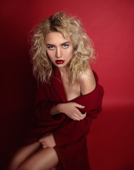 Beautiful portrait seductive woman with light blond hair,blue eyes and red lips posing in red coat and on dark red background. Fashion, glamour, concept