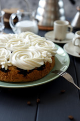 Close up of homemade cake with coconut cream swirls served with coffee on dark background copy space. Still life with natural lighting