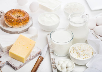 Fresh dairy products in vintage wooden box on white table background. Jar and glass of milk, bowl of sour cream and cheese and eggs. Fresh baked bagel on round chopping board with knife.