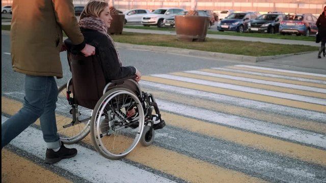 Man pushing the wheelchair with handicapped girlfriend across the street