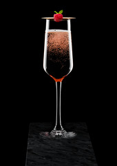 Elegant glass of pink rose champagne with raspberry on stick on black marble board on black background.Space for text