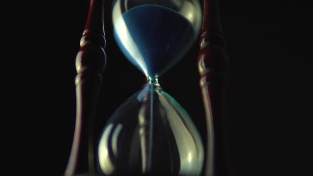 Sand glass grains in the hourglass. Still hour glass close up over black background, transience of time concept. Time of all liveable things idea.