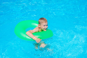 Fototapeta na wymiar Happy kid boy having fun in an swimming pool. Active happy healthy preschool child learning to swim. With safe floaties or swimmies.