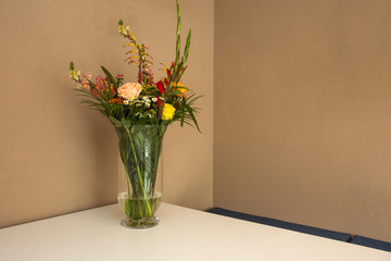 Beautiful flower bouquet on white table with light brown wall, space for text