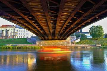 Long exposure image of a small boat passing through the Neris River under the Green Bridge in Vilnius, Lithuania.