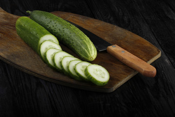fresh cucumber on wooden cutting board with knife isolated on black background