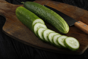fresh cucumber on wooden cutting board with knife isolated on black background