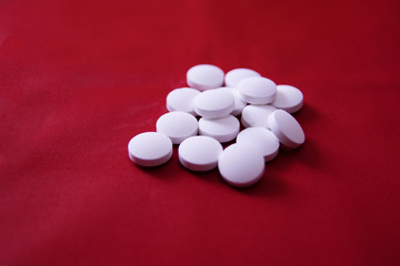 White round medical pills scattered in a pile on a red background.
