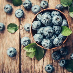 Freshly picked blueberries in wooden bowl on wooden background. Healthy eating and nutrition.