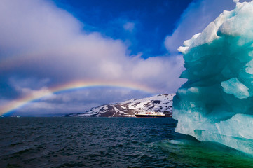 Fototapeta na wymiar Cruise ship under a rainbow cruising past an iceberg in Hornsund Svalbard Norway within the arctic circle.