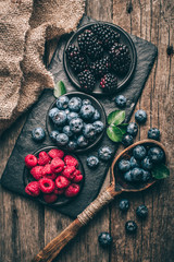 Fresh berries with raspberries, blueberries, blackberries in bowl on a stone stand on wood background.