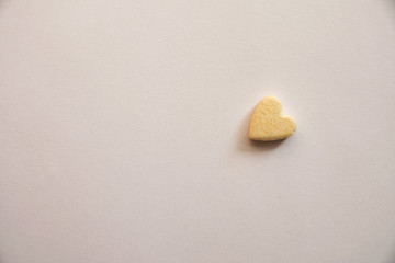Yellow pill in the form of a heart lies alone on a white background leaving an empty space